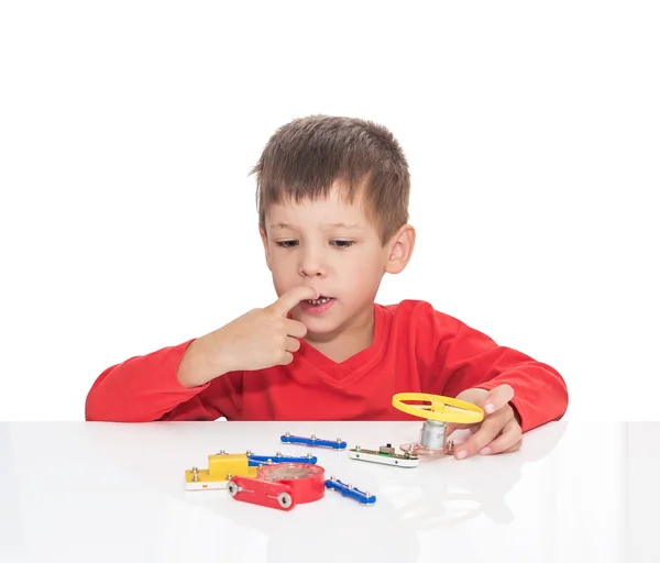 Der fünfjährige Junge sitzt an einem weißen Tisch und spielt einen elektronischen Designer — Stockfoto