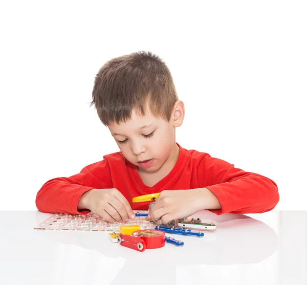 The five-year-old boy sits at a white table and plays an electronic designer — Stock Photo, Image