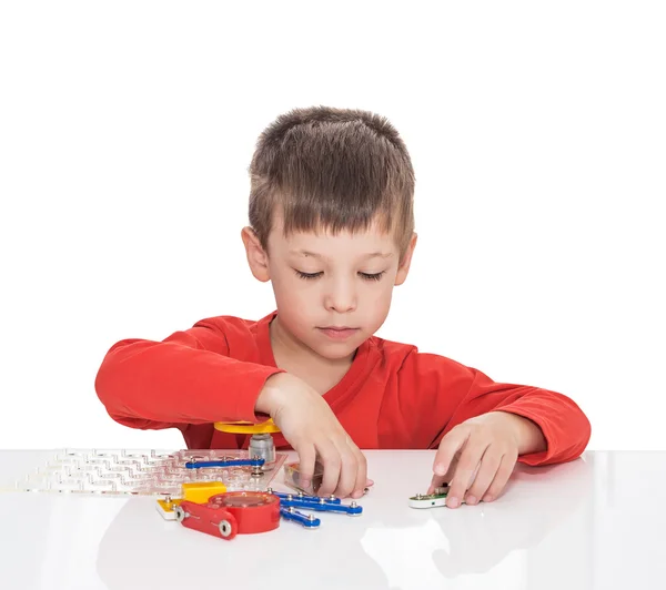 The five-year-old boy sits at a white table and plays an electronic designer — Stock Photo, Image