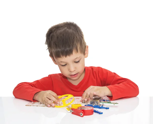 De vijf-jaar-oude jongen zit aan een tafel met witte en speelt een elektronische ontwerper — Stockfoto