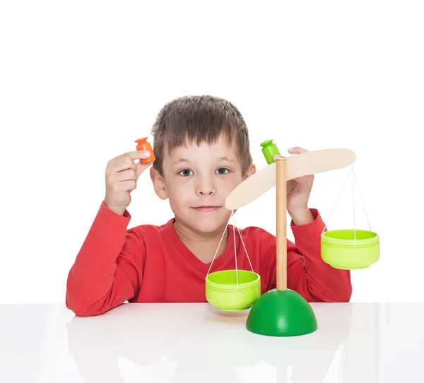 The five-year-old boy sits at a white table and plays with wooden scales — Stock Photo, Image