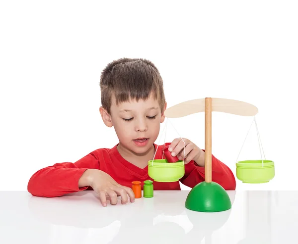 Пятилетний мальчик сидит за белым столом и играет с деревянными весами — стоковое фото