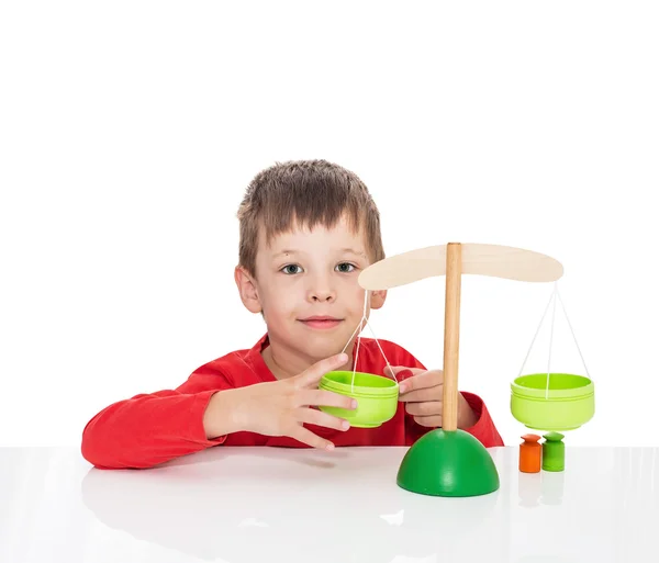 Der fünfjährige Junge sitzt an einem weißen Tisch und spielt mit Holzwaagen — Stockfoto