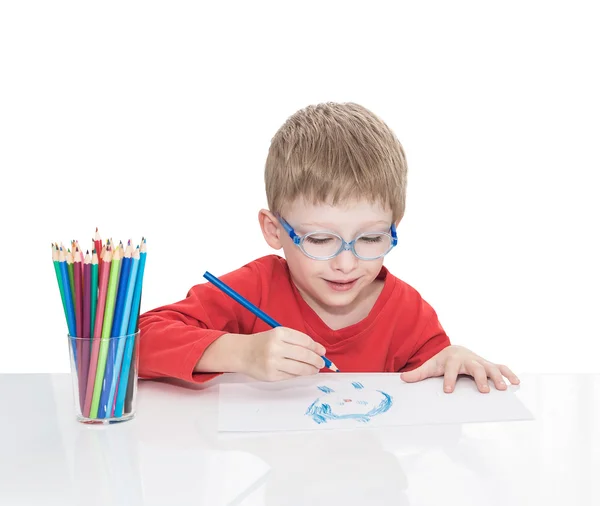 The five-year-old boy in blue points sits at a white table and and draws pencils — Stock Photo, Image