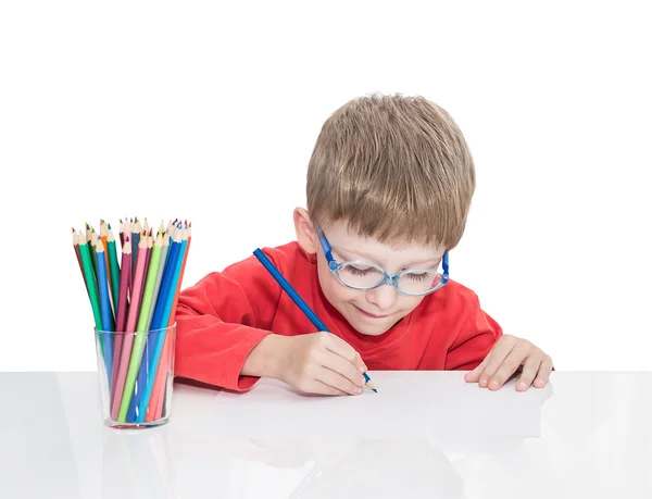 П'ятирічний хлопчик у блакитних точках сидить за білим столом і малює олівці — стокове фото