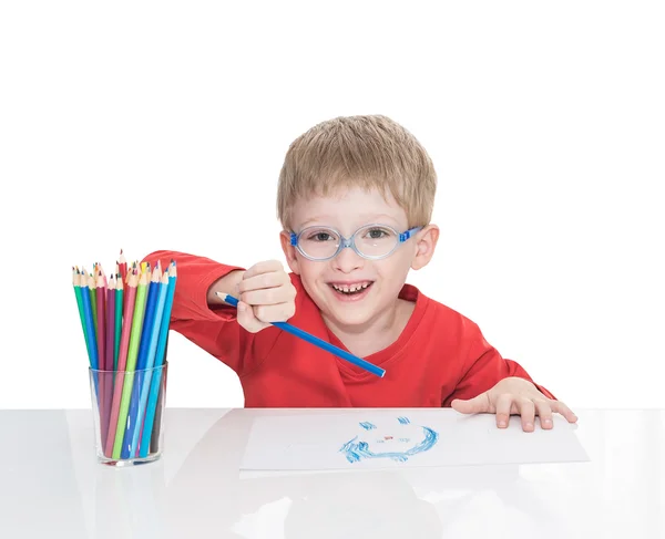 The five-year-old boy in blue points sits at a white table and and draws pencils — Stock Photo, Image