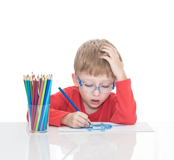 П'ятирічний хлопчик у блакитних точках сидить за білим столом і малює олівці — стокове фото