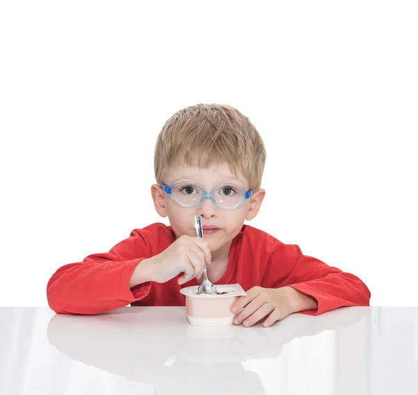 Το πέντε-έτος-παλαιό αγόρι κάθεται σε ένα άσπρο τραπέζι και τρώει γιαούρτι — Φωτογραφία Αρχείου