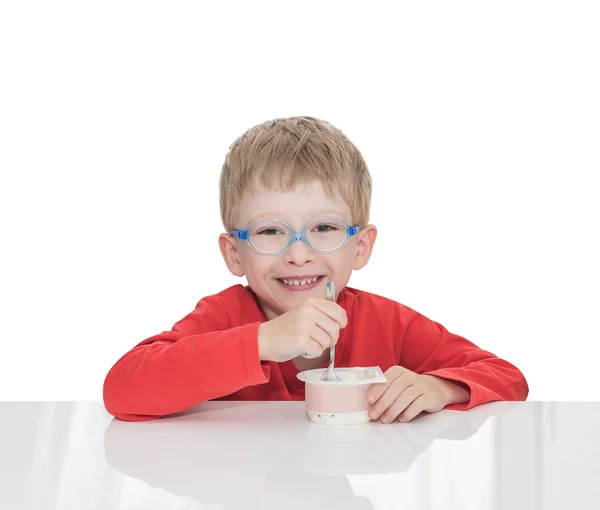 El niño de cinco años se sienta en una mesa blanca y come yogur. —  Fotos de Stock