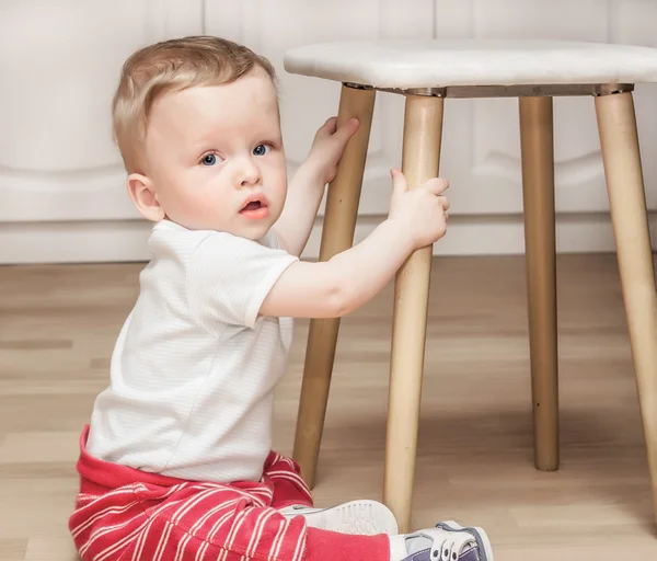 Dziecko siedzi na podłodze w pobliżu stołek — Zdjęcie stockowe