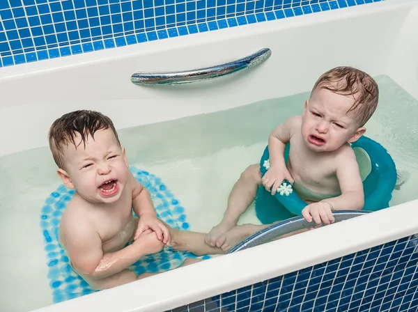 Two-year-old twins children sit in a bath, one cries, another plays — Stock Photo, Image