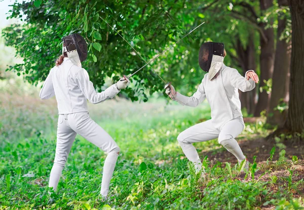 Two rapier fencer women fighting over beautiful nature park back — Stock Photo, Image