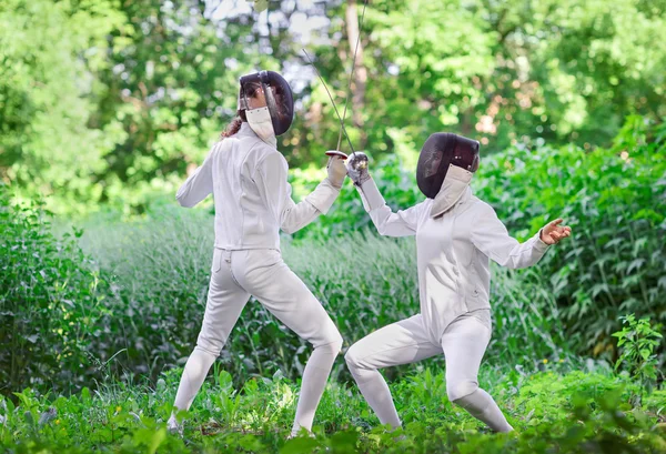 Two rapier fencer women fighting over beautiful nature park back — Stock Photo, Image