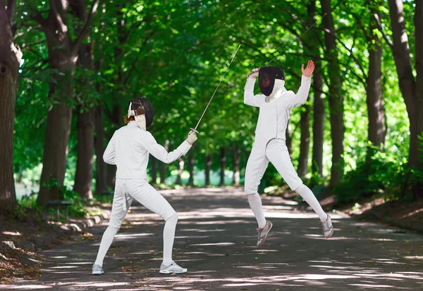 Two rapier fencer women fighting over park alley, attacking each — Stock Photo, Image