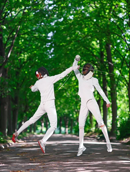 Two rapier fencer women fighting over park alley, attacking each — Stock Photo, Image