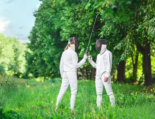 Dos esgrimistas mujeres que se quedan en el parque con rapiers cruzados Imagen de archivo