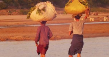 Burma'nın kırsal kesiminde irrawaddy nehrini geçerken birmanyalı kadınlar kafalarında yük taşıyorlar.