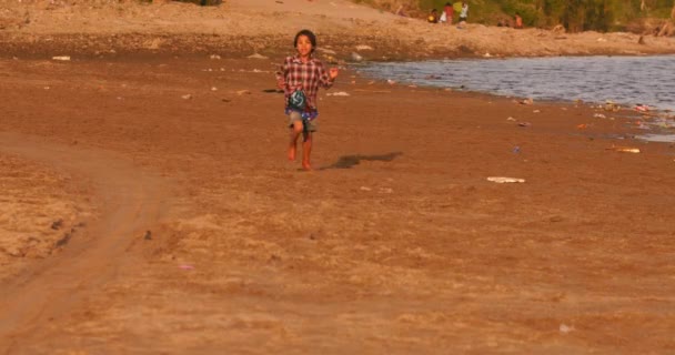 Speelse Birmese jongen die langs Irrawaddy River Shore loopt bij zonsondergang — Stockvideo