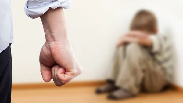 Angry man raised fist over wall corner sitting child boy — Stock Photo, Image