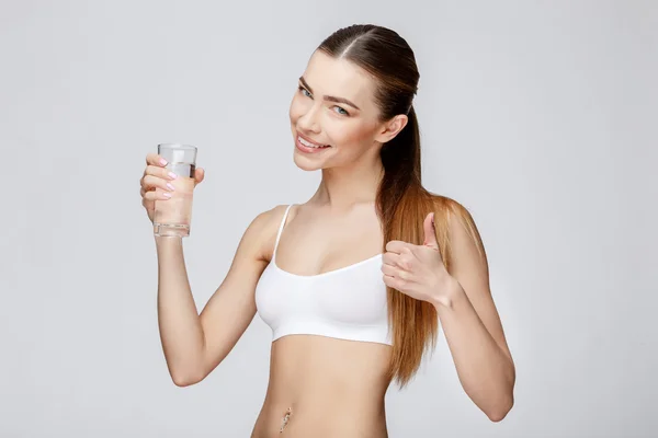Donna sportiva su sfondo grigio con un bicchiere d'acqua — Foto Stock