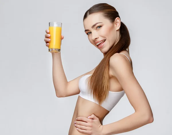 Mulher desportiva sobre fundo cinza segurando vidro de suco de laranja — Fotografia de Stock