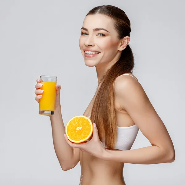 Mulher desportiva sobre fundo cinza segurando vidro de suco de laranja — Fotografia de Stock