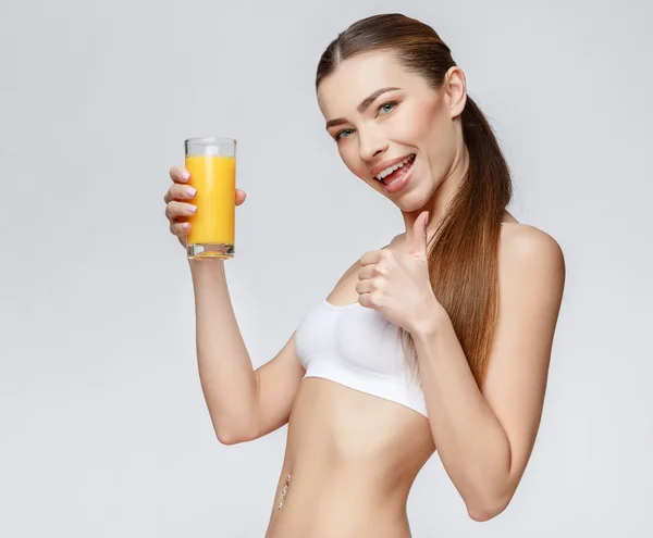 Mujer deportiva sobre fondo gris sosteniendo vaso de jugo de naranja —  Fotos de Stock