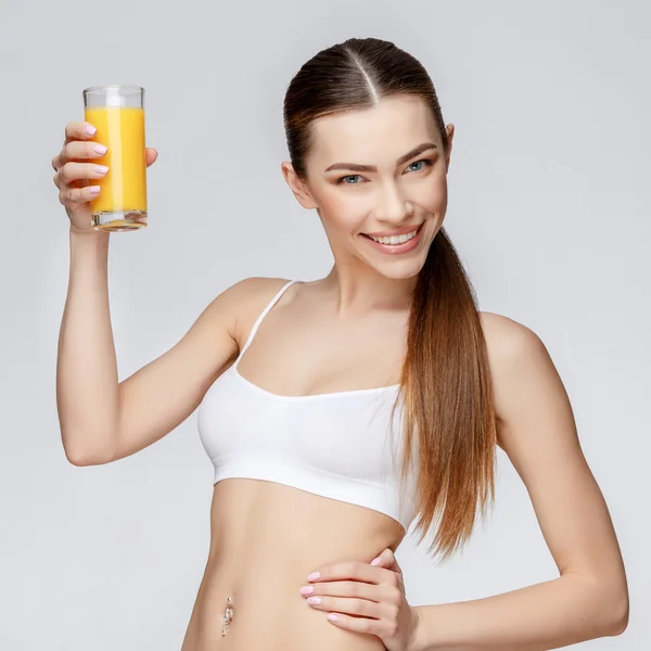 Sporty woman over gray background holding glass of orange juice — Stock Photo, Image