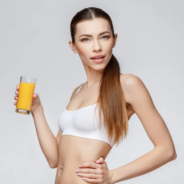 Sportieve vrouw over grijze achtergrond met glas sinaasappelsap — Stockfoto