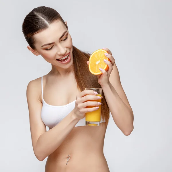 Sportig kvinna över grå bakgrund hålla glas apelsinjuice — Stockfoto