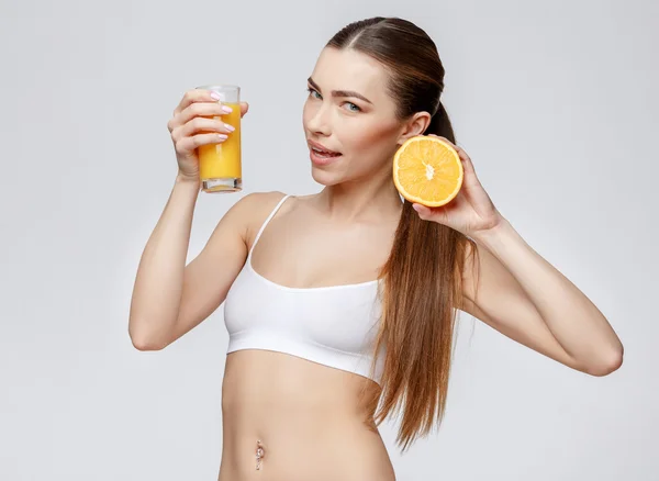 Mulher desportiva sobre fundo cinza segurando vidro de suco de laranja — Fotografia de Stock