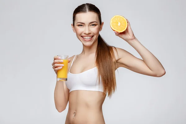 Mulher desportiva sobre fundo cinza segurando vidro de suco de laranja — Fotografia de Stock