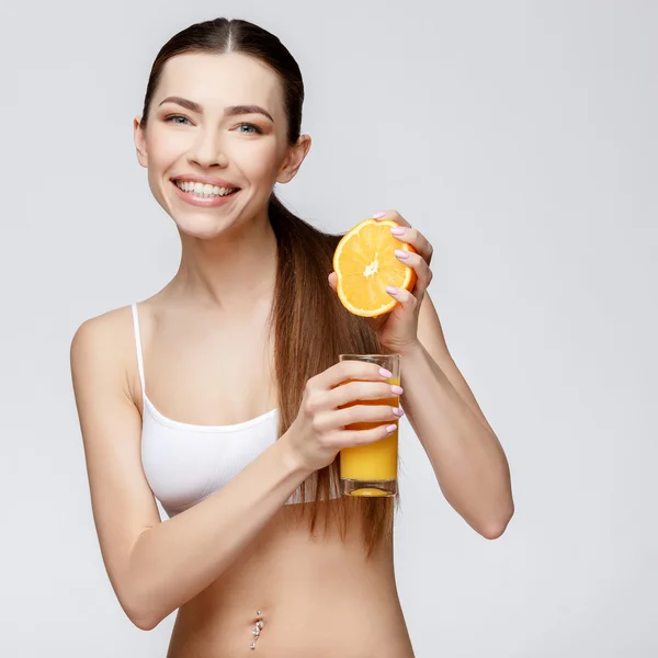 Donna sportiva su sfondo grigio con un bicchiere di succo d'arancia — Foto Stock