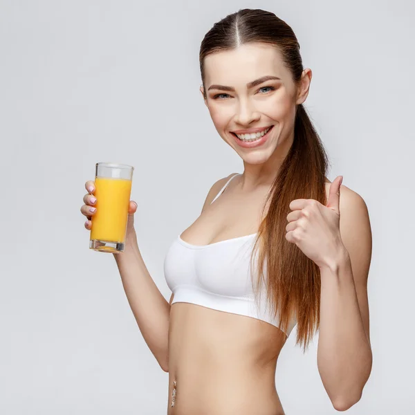 Mujer deportiva sobre fondo gris sosteniendo vaso de jugo de naranja —  Fotos de Stock