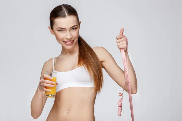 Sportig kvinna över grå bakgrund hålla glas apelsinjuice — Stockfoto