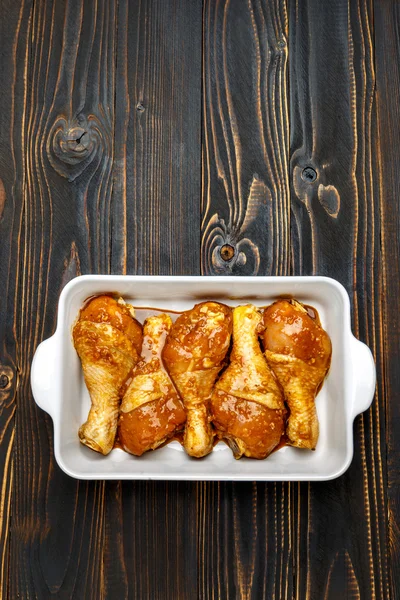 Gambe di pollo crude in teglia su uno sfondo di legno — Foto Stock