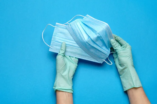 Mano humana en guantes protectores que sostienen la máscara protectora facial aislada sobre fondo azul — Foto de Stock