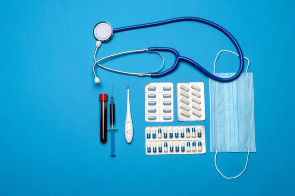 Prevence a léčba koncepce koronavirové zdravotní péče - injekční stříkačka, maska, tablety, stetoskop a Covid-19 zkumavka na modrém pozadí — Stock fotografie