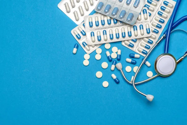 Egészségügyi ellátás vagy betegség koncepció - sztetoszkóp és tabletták kék alapon — Stock Fotó