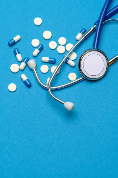 Egészségügyi ellátás vagy betegség koncepció - sztetoszkóp és tabletták kék alapon — Stock Fotó