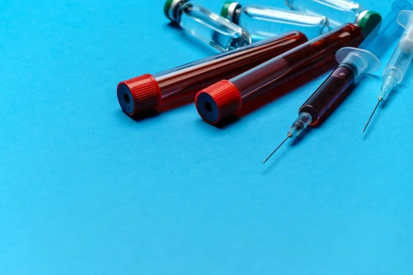 Шприц, пробирки с образцами крови и ампулы с лекарствами или вакциной на синем фоне — стоковое фото