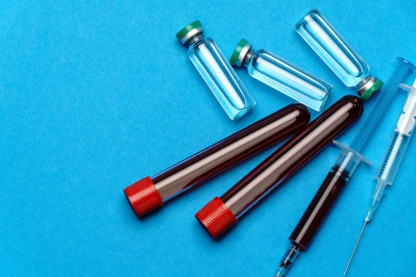 Seringa, tubos de ensaio com amostras de sangue e ampolas com medicamentos ou vacina sobre fundo azul — Fotografia de Stock