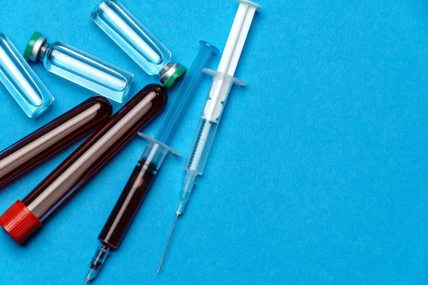Fecskendő, vérmintákkal ellátott kémcsövek és ampullák gyógyszerekkel vagy vakcinával kék alapon — Stock Fotó