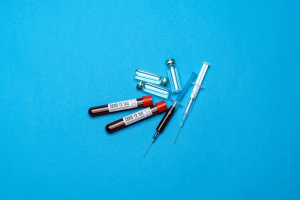 Seringue, éprouvettes avec échantillons de sang et ampoules avec médicaments ou vaccin sur fond bleu — Photo