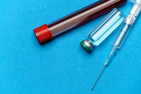 Fecskendő, vérmintákkal ellátott kémcsövek és ampullák gyógyszerekkel vagy vakcinával kék alapon — Stock Fotó