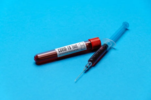 Syringe And Plastic Test Tube With Blood Sample over blue background with copyspace — Stock Photo, Image