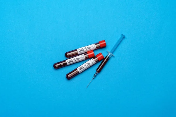 Seringa e tubo de teste de plástico com amostra de sangue sobre fundo azul com copyspace — Fotografia de Stock