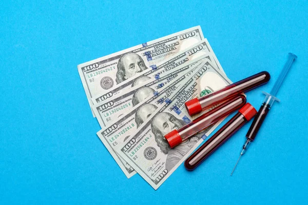 Cierre hasta 100 billetes de dólar y muestra de sangre en tubo de ensayo sobre fondo azul —  Fotos de Stock