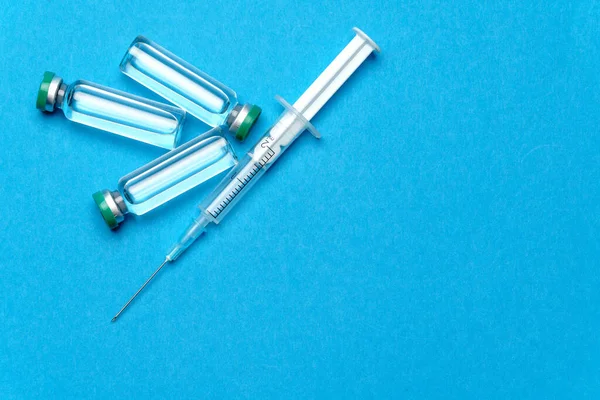Syringe and ampoules with medicines or vaccine over blue background — Stock Photo, Image
