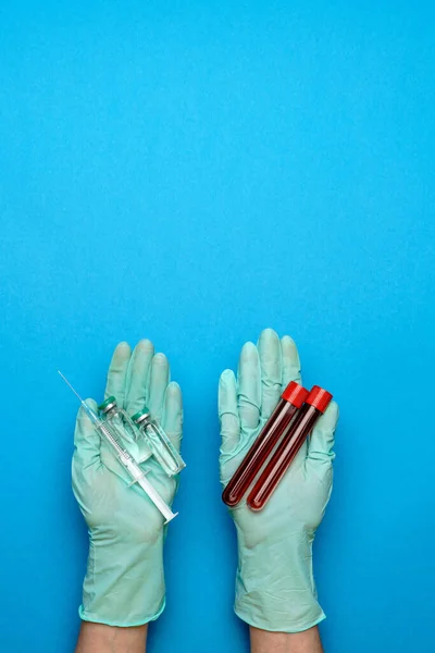 Лаборант-ассистент или врач в резиновых или латексных перчатках держит ампулу с лекарством или вакциной и пробирку с образцом крови — стоковое фото